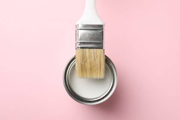 Paint can and brush on pink background, top view